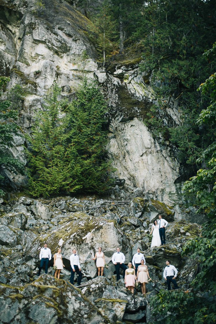 Wedding party posed on dramatic rocky cliff face surrounded by evergreen trees.