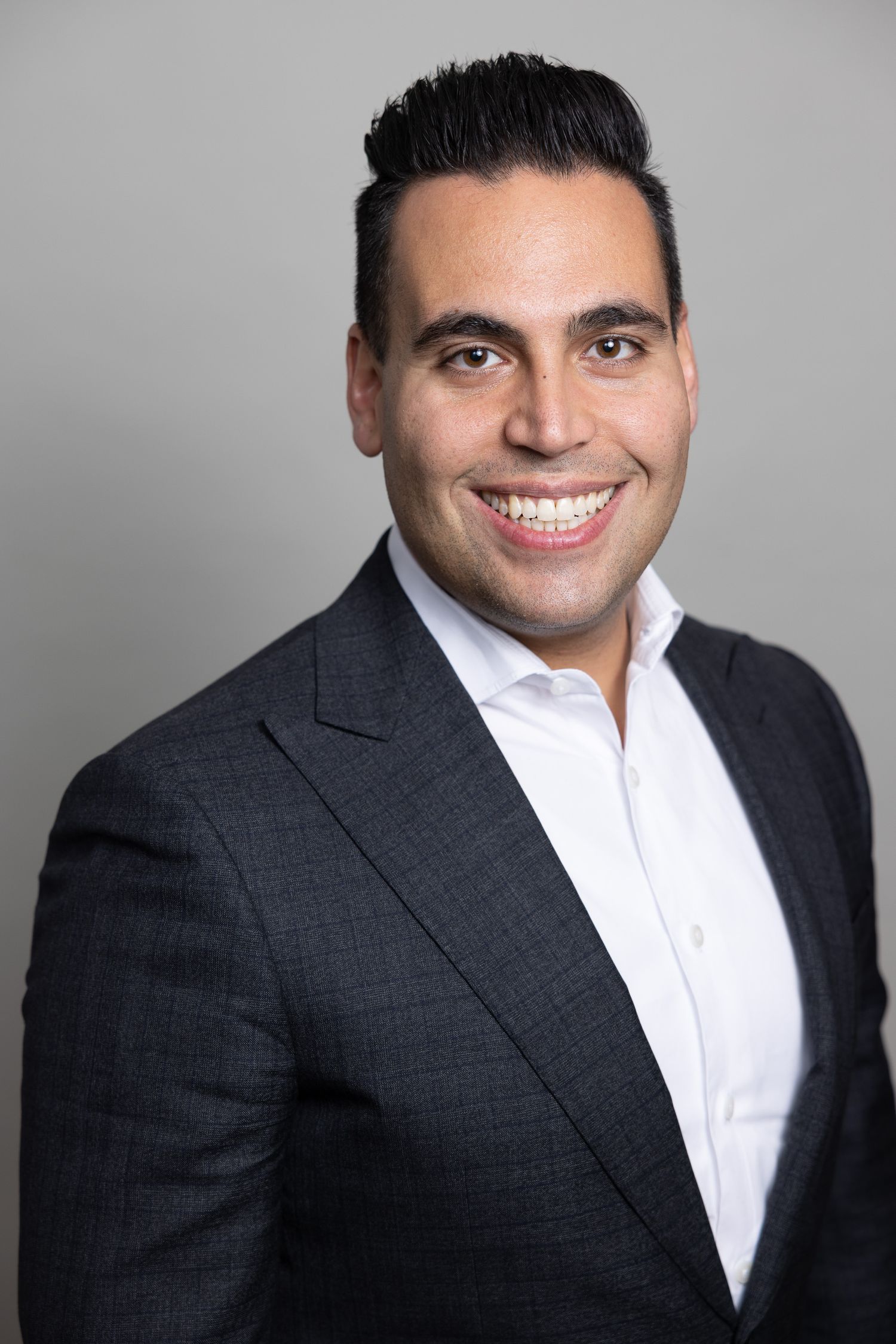 Corporate headshot of a person in a dark suit and white shirt with a bright smile.