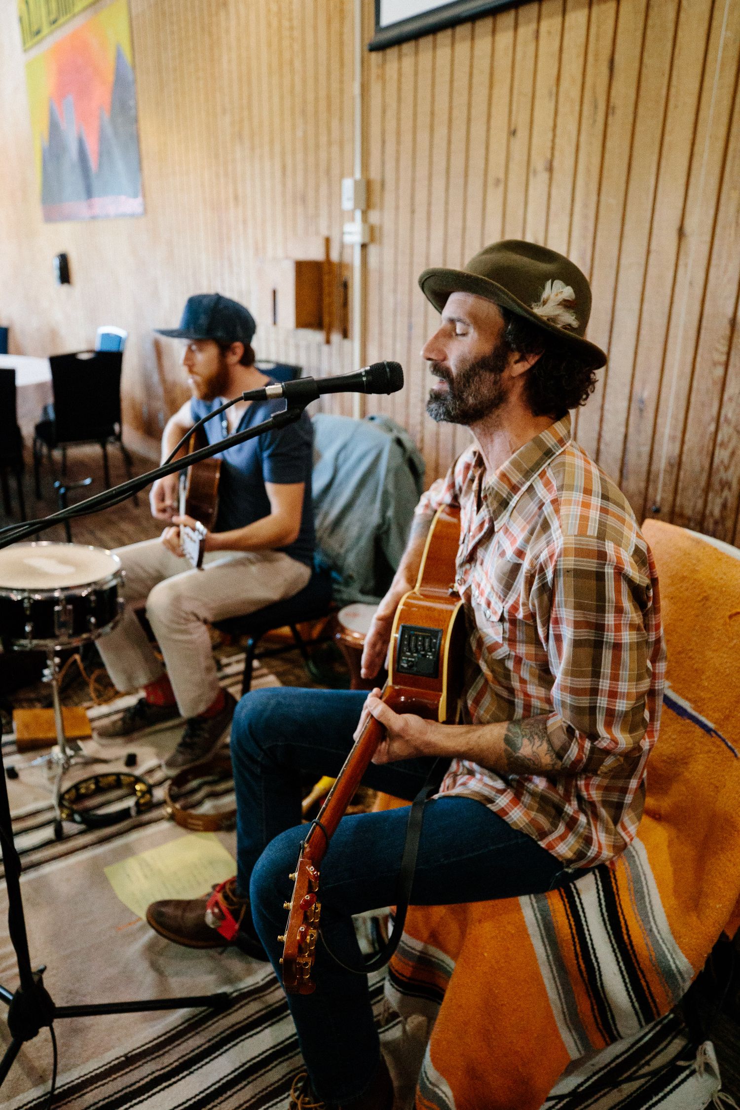 Musicians perform in a rustic studio setting with acoustic guitar and drums.