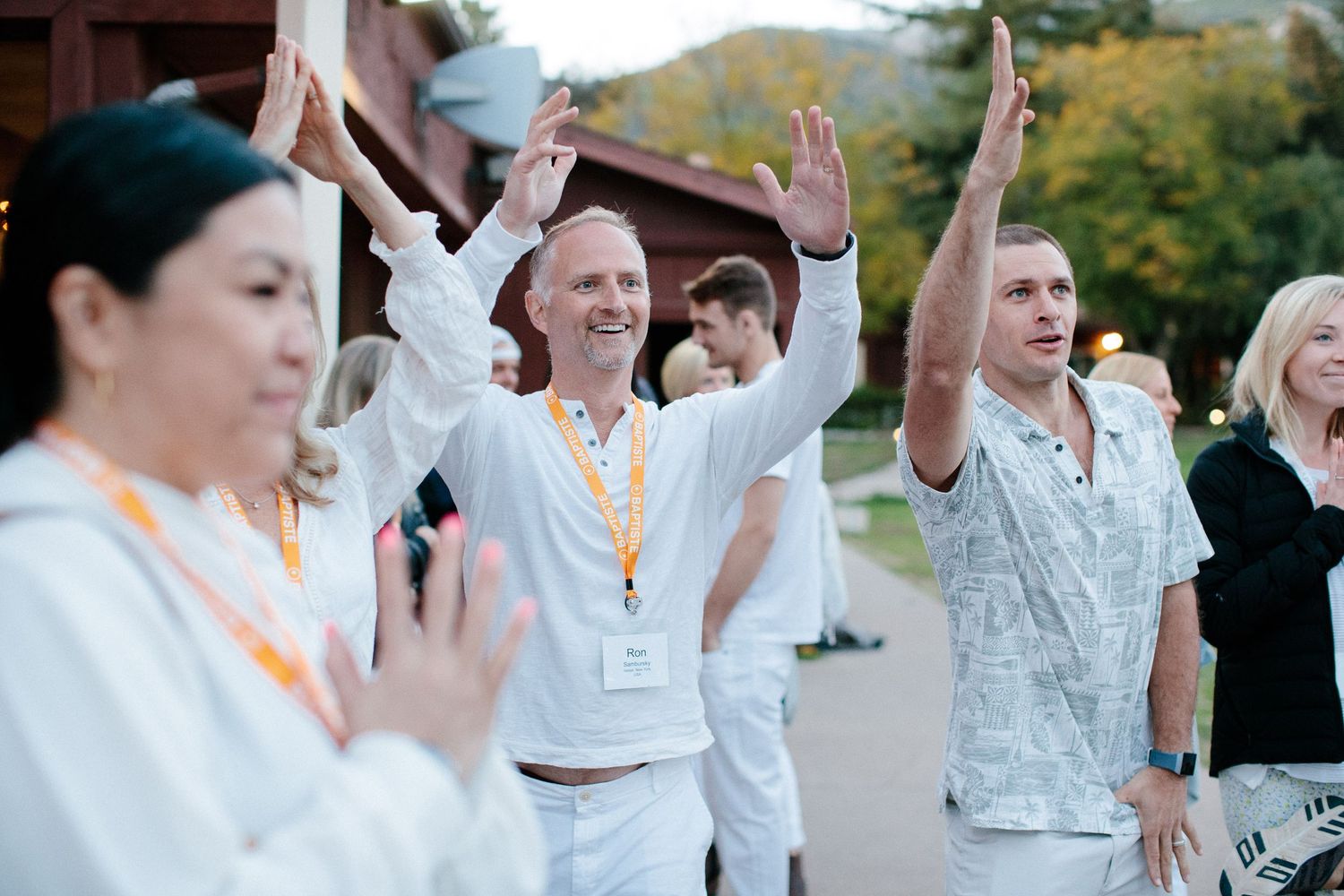 People dressed in white raise their hands in unison during an outdoor group activity.