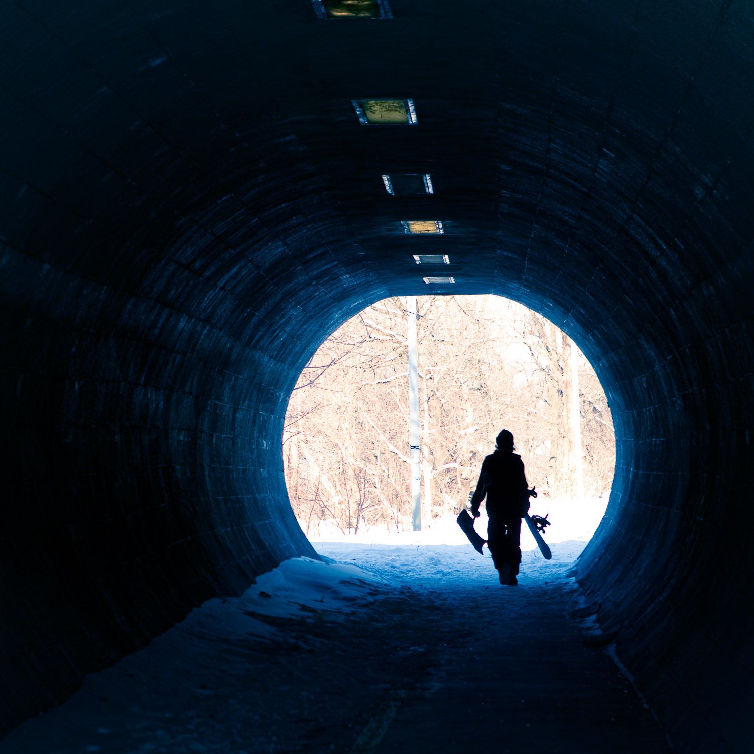 Silhouetted figures walk through a dark tunnel with bright light at the end creating a dramatic contrast effect.