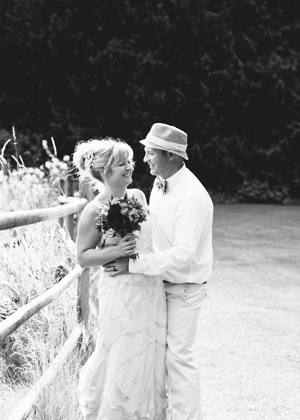 A romantic black and white series of photos showing a couple embracing against a white fence in a field.