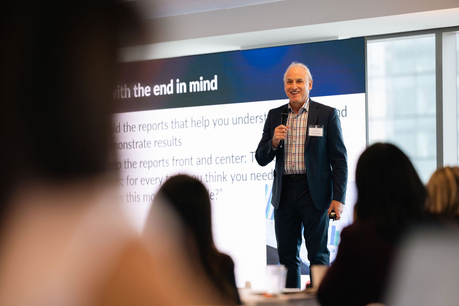A presenter speaks at a business conference while standing in front of a large projection screen.
