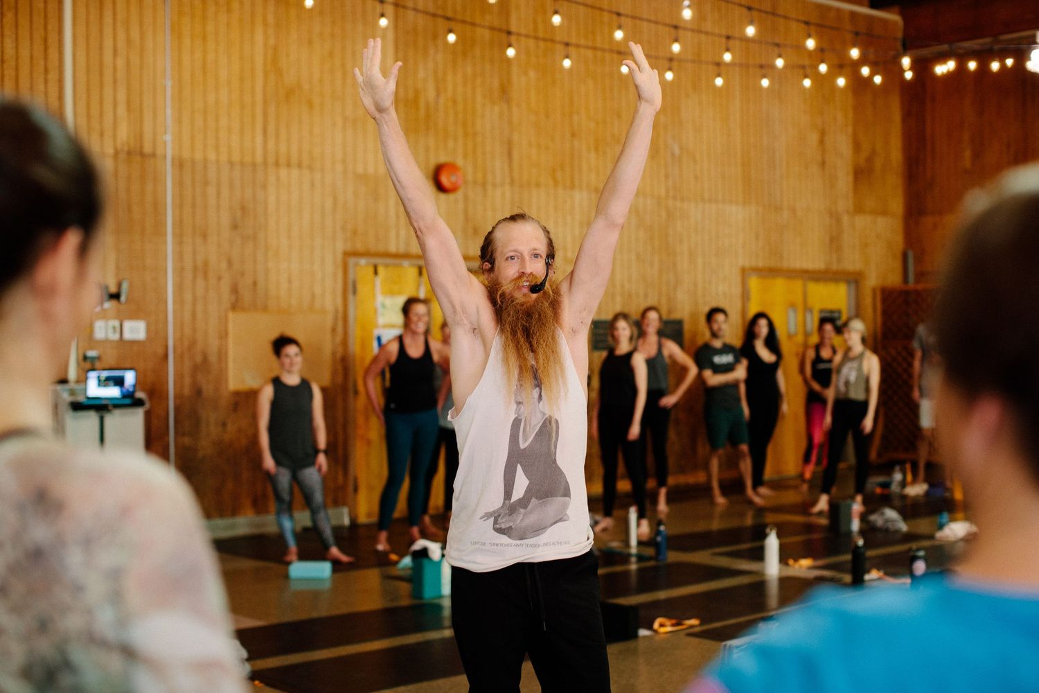 A person with long hair and a gray tank top raises their arms during a group activity.