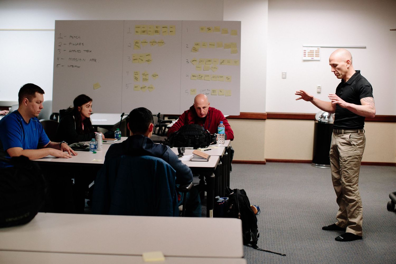 Group discussion in a classroom with a whiteboard and instructor gesturing during presentation.
