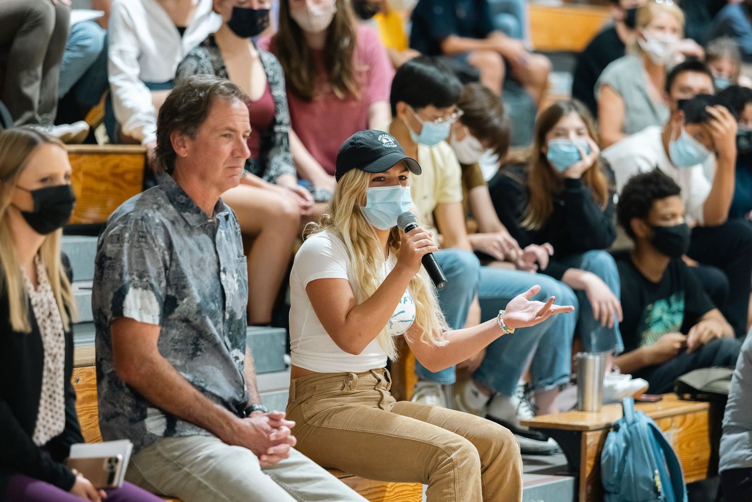 Audience members wearing masks watch intently during indoor event.