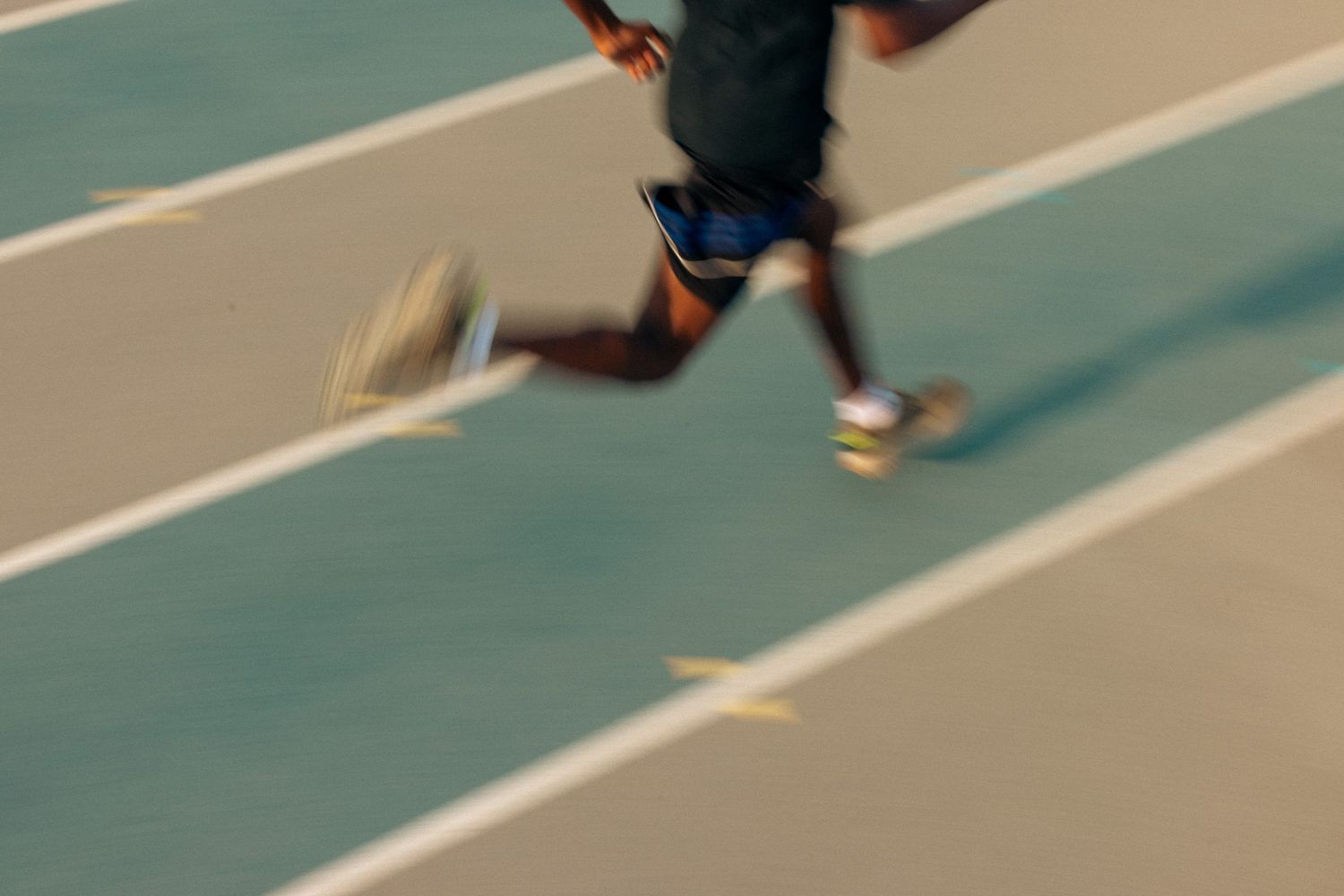 Athletes compete in an indoor track meet, running on a blue synthetic track surface in parallel lanes.