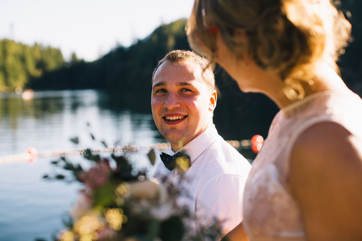 A groom in bow tie smiles during lakeside wedding celebrations.