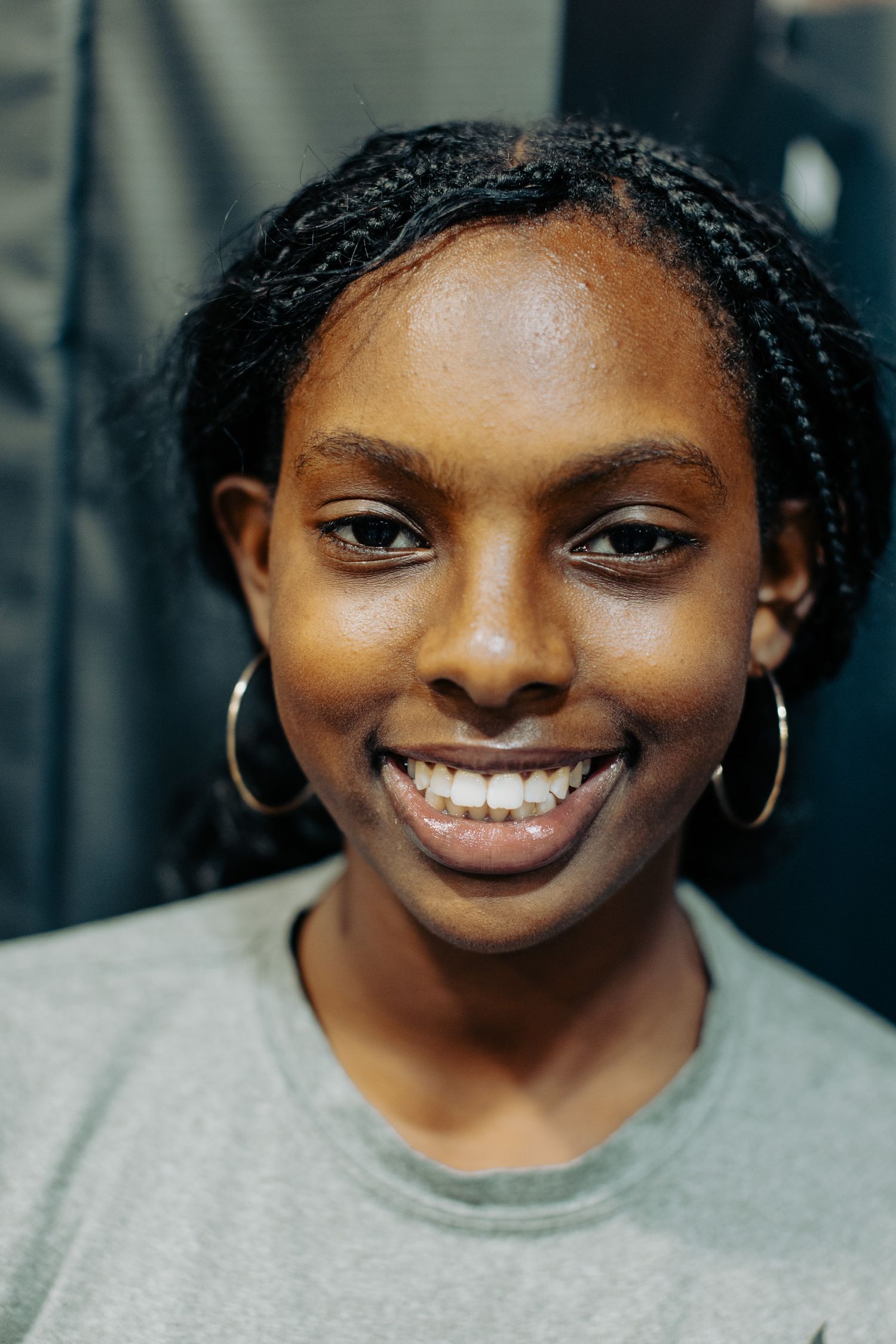 A bright and joyful smile radiates warmth while wearing casual gray attire and hoop earrings.