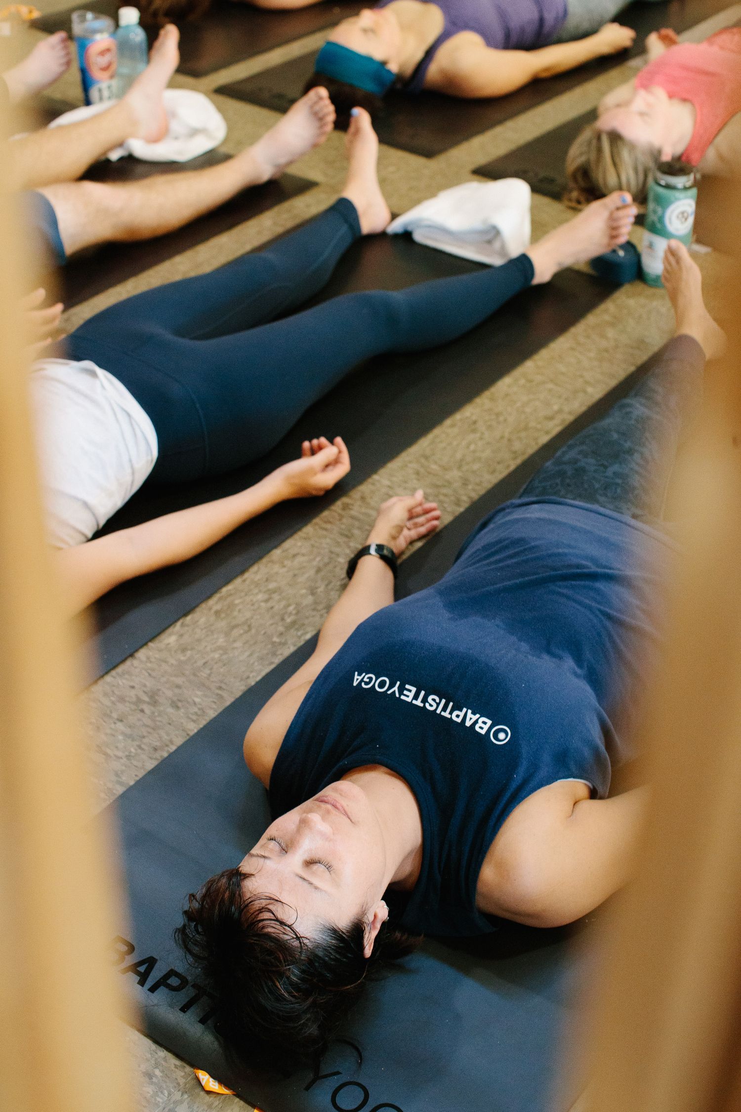 Participants lying on their backs practicing relaxation techniques during a yoga class on exercise mats.