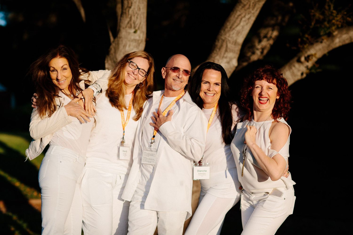 A group wearing white clothing poses together outdoors for a celebratory photo.