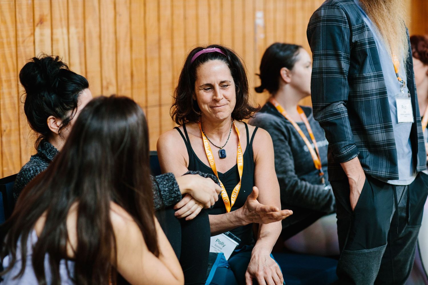 A group of people engaged in casual conversation while sitting against a wooden wall.
