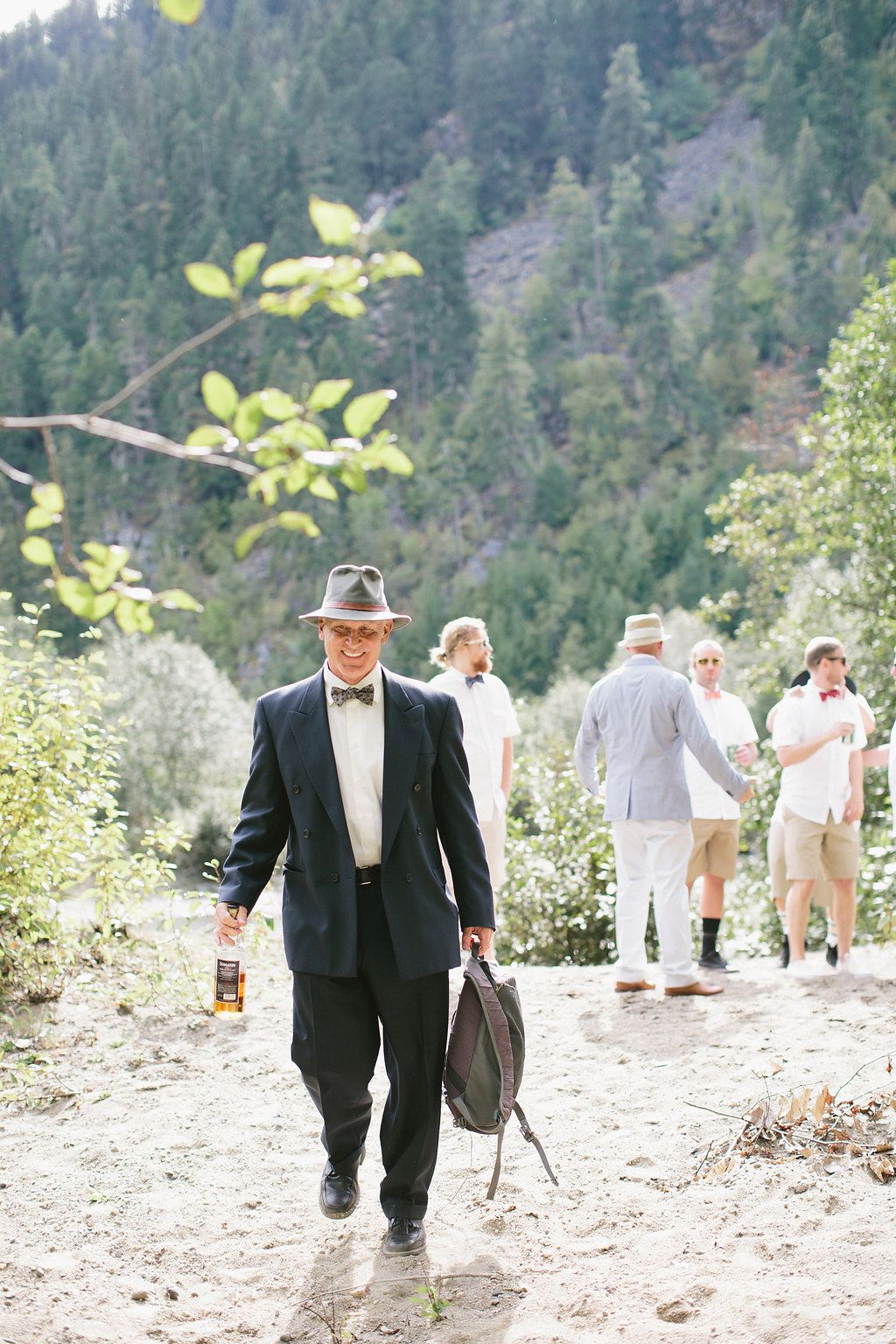 Wedding guests walking along a mountain path with evergreen trees in the background.