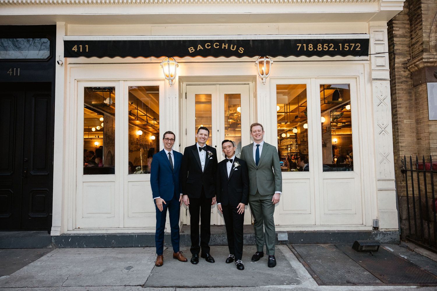 Four men in formal attire posing outside Bacchus restaurant in Brooklyn, NY, celebrating a wedding.