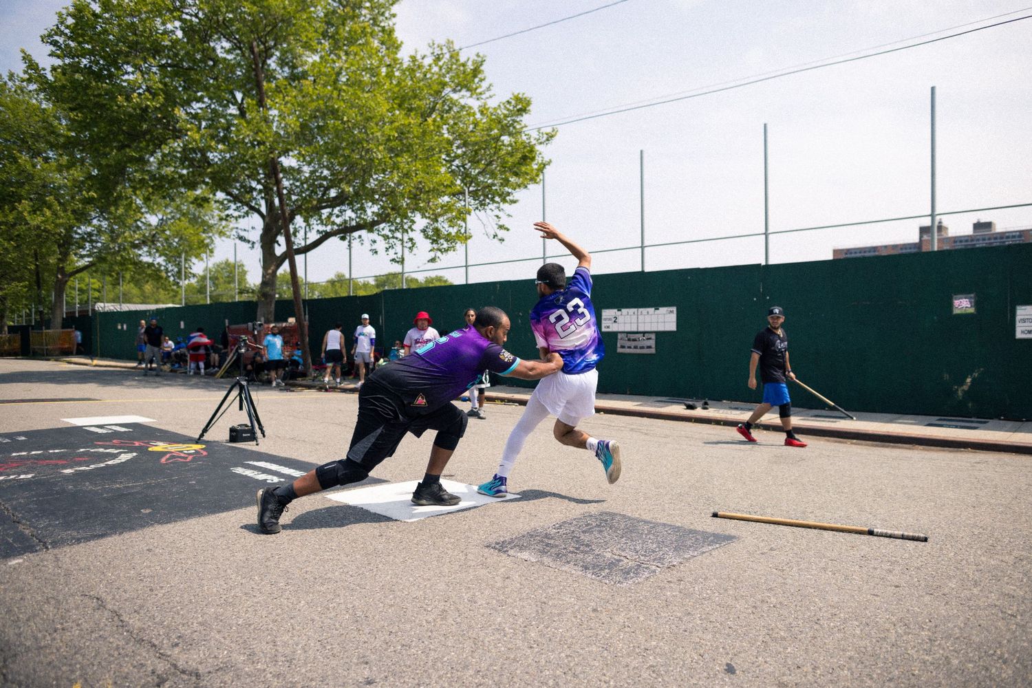 Baseball player swings at pitch while catcher crouches behind home plate during outdoor game.