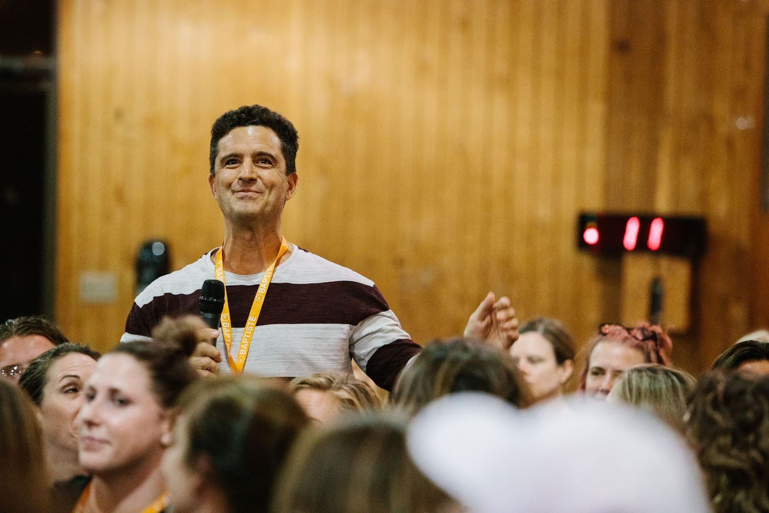 Audience member standing among crowd during indoor event looking upward with enthusiasm.