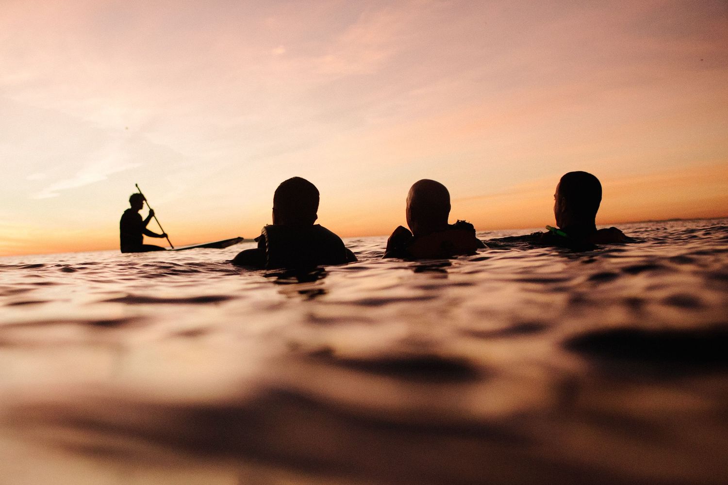 Silhouettes of swimmers in ocean water during sunset creating a serene scene.