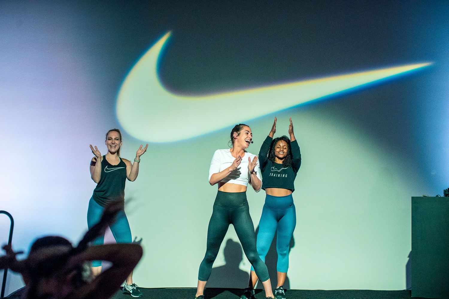 Dancers performing against a large illuminated Nike swoosh logo projection.