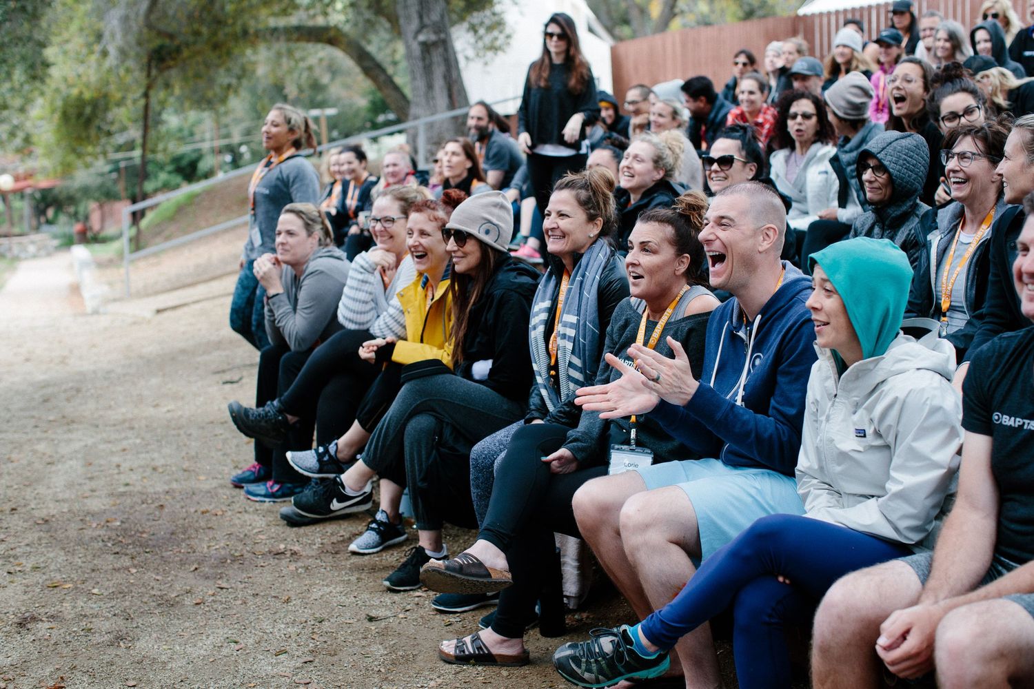 A crowd of spectators sitting outdoors laughing and enjoying an event together in a natural setting.