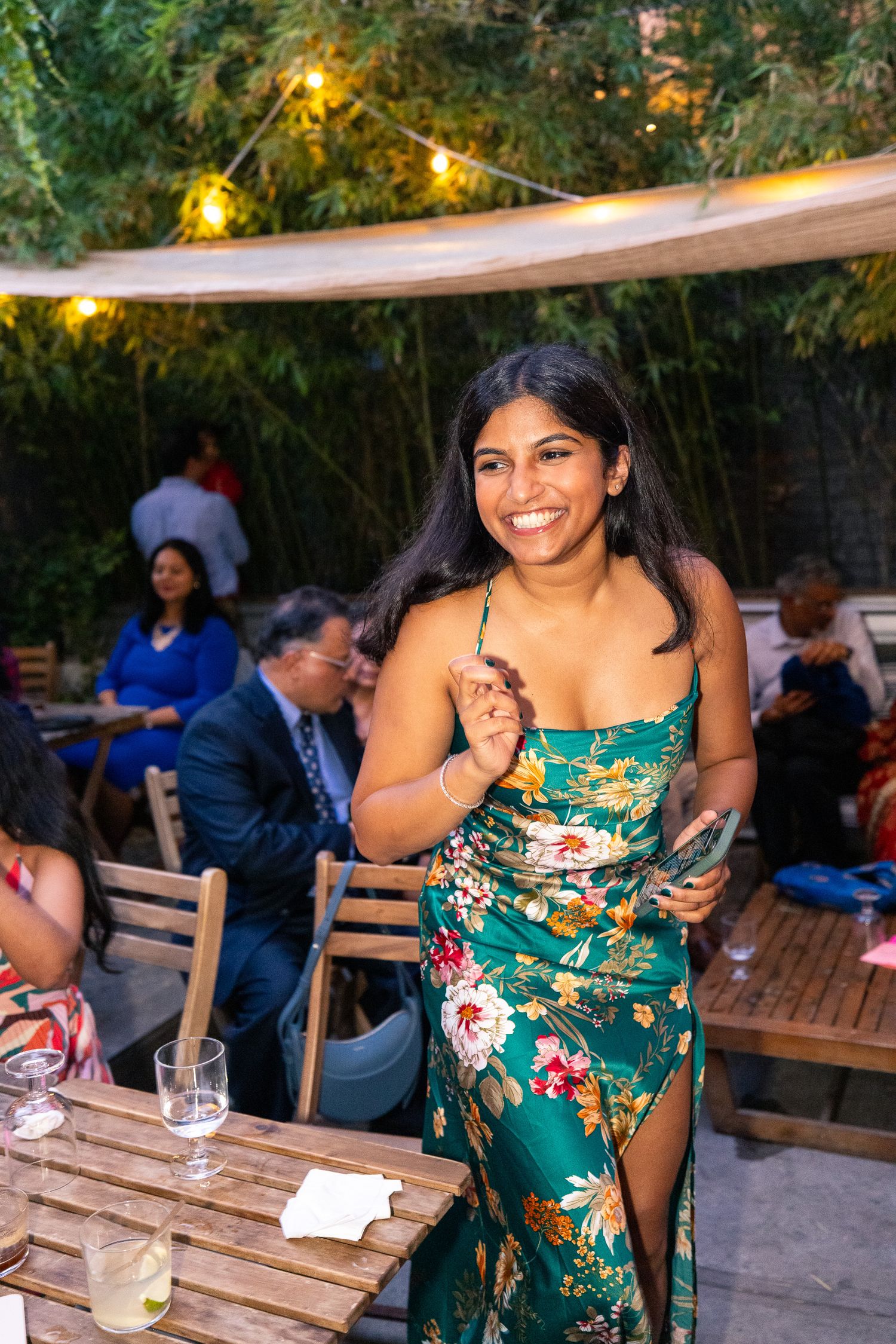 A woman in a floral dress smiles while standing at an outdoor party with string lights.