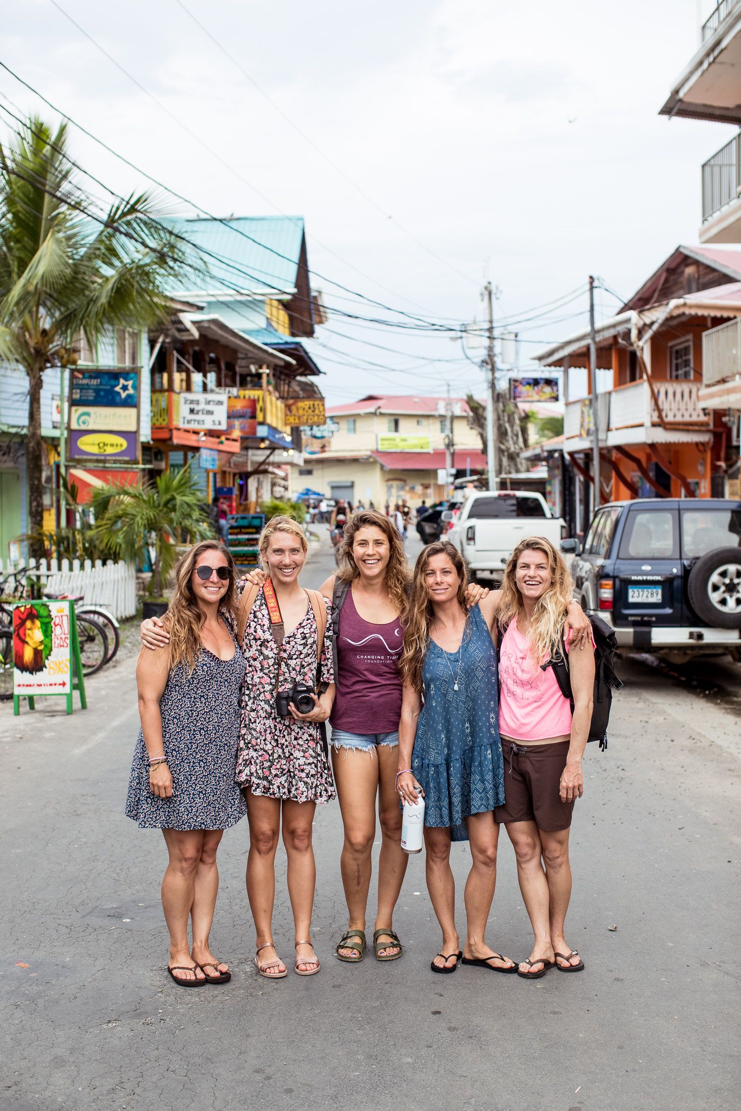 A group poses on a tropical street with palm trees and shops in the background.
