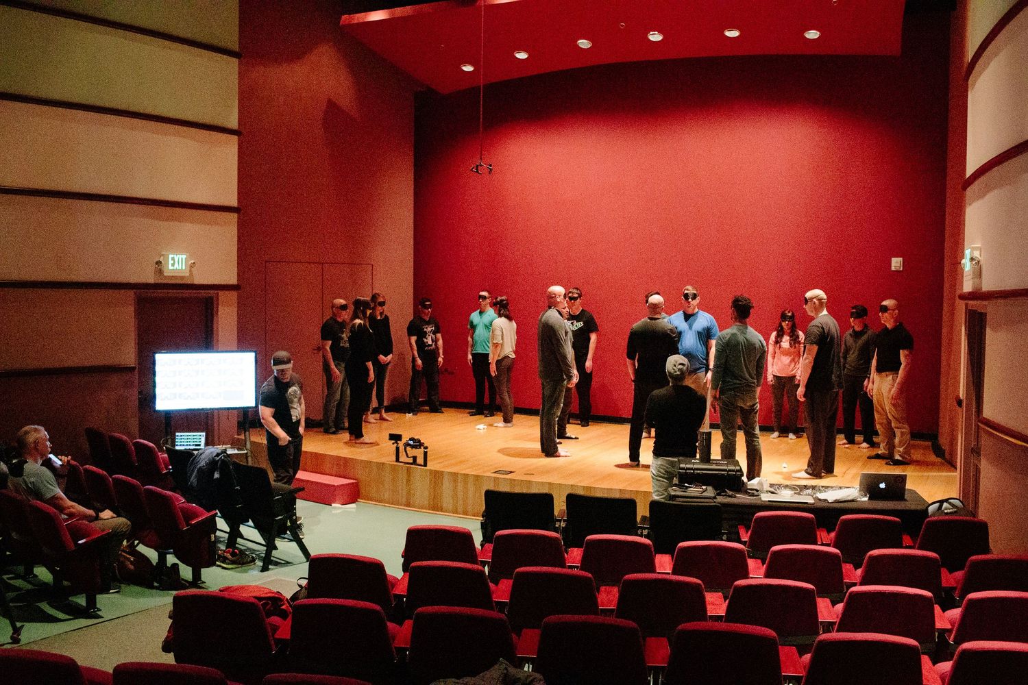 Group presentation in an auditorium with red seats and lighting during performance or training.