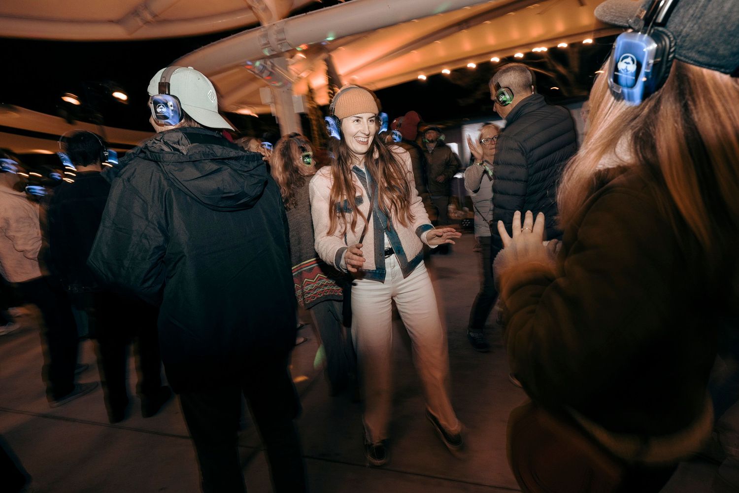 Crowd dancing at indoor party with headphones and ambient lighting.