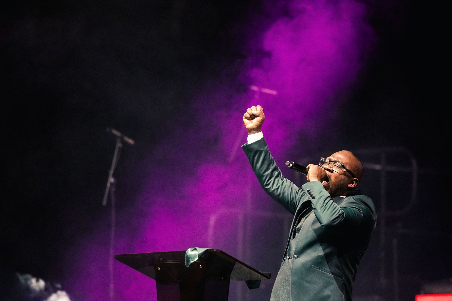 A performer sings passionately on stage with dramatic purple lighting and fog effects during a live concert performance.