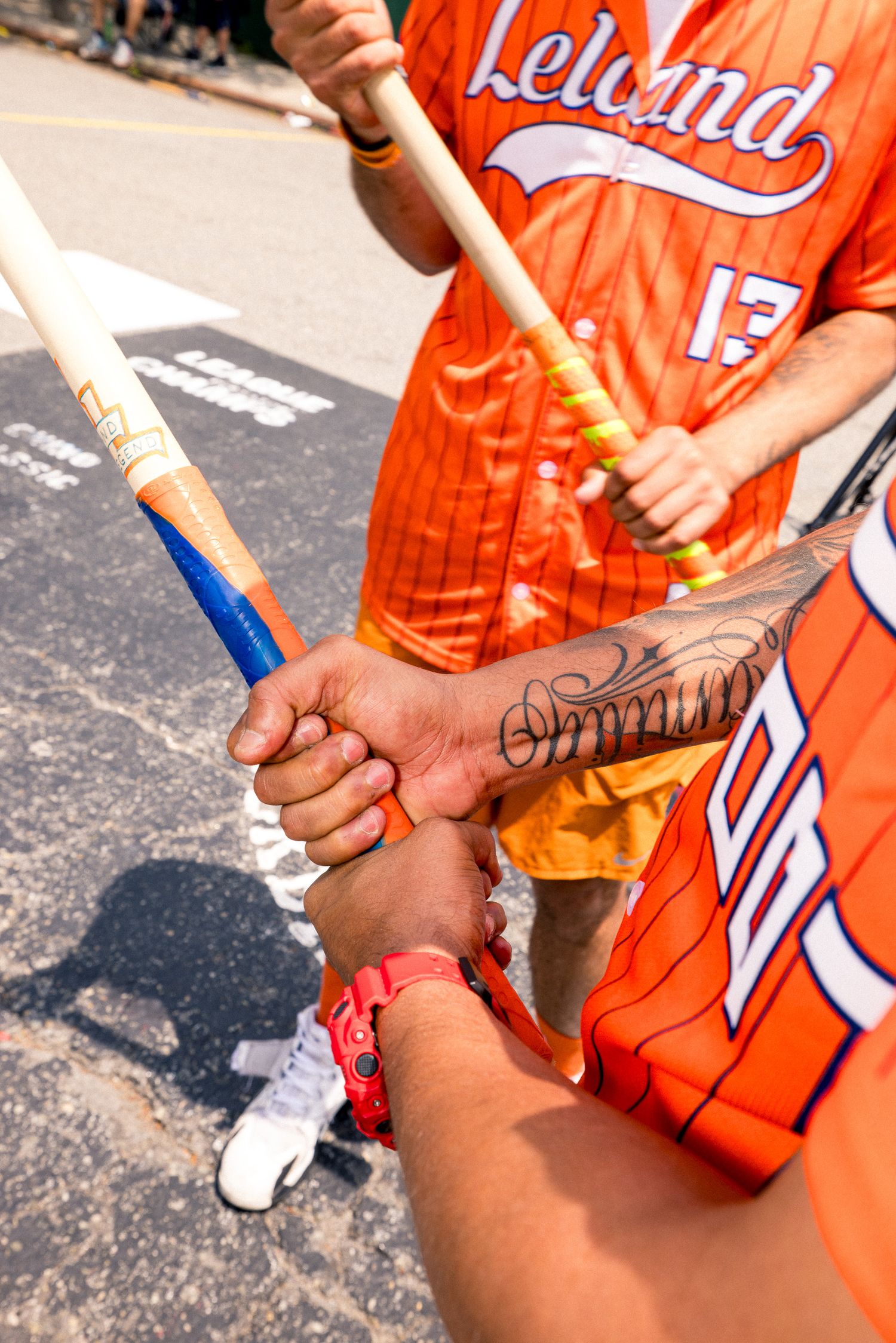 Close-up shots of players in orange jerseys signing autographs on baseball equipment outdoors.