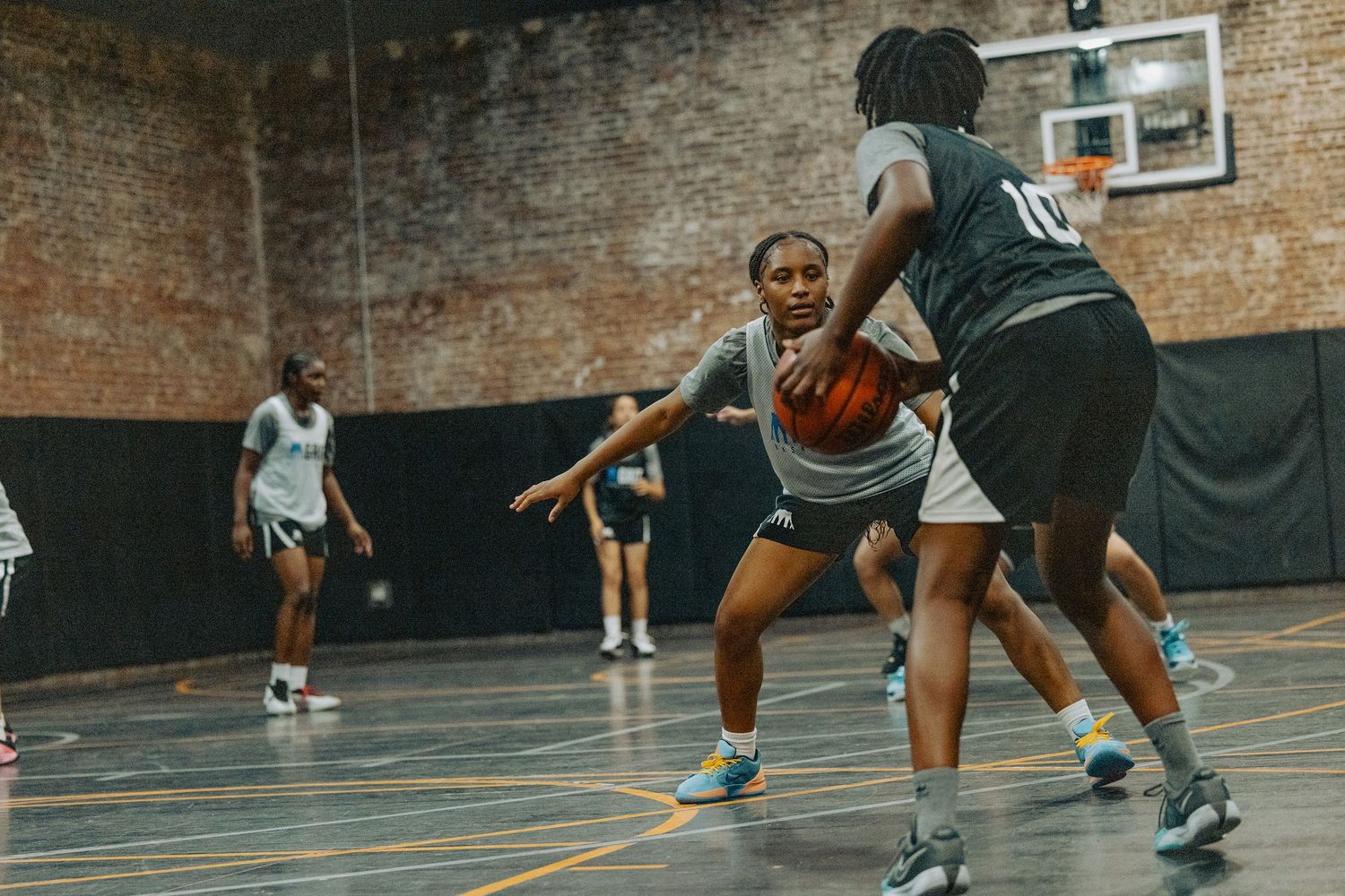 Players engaged in competitive basketball game on indoor court with brick walls.