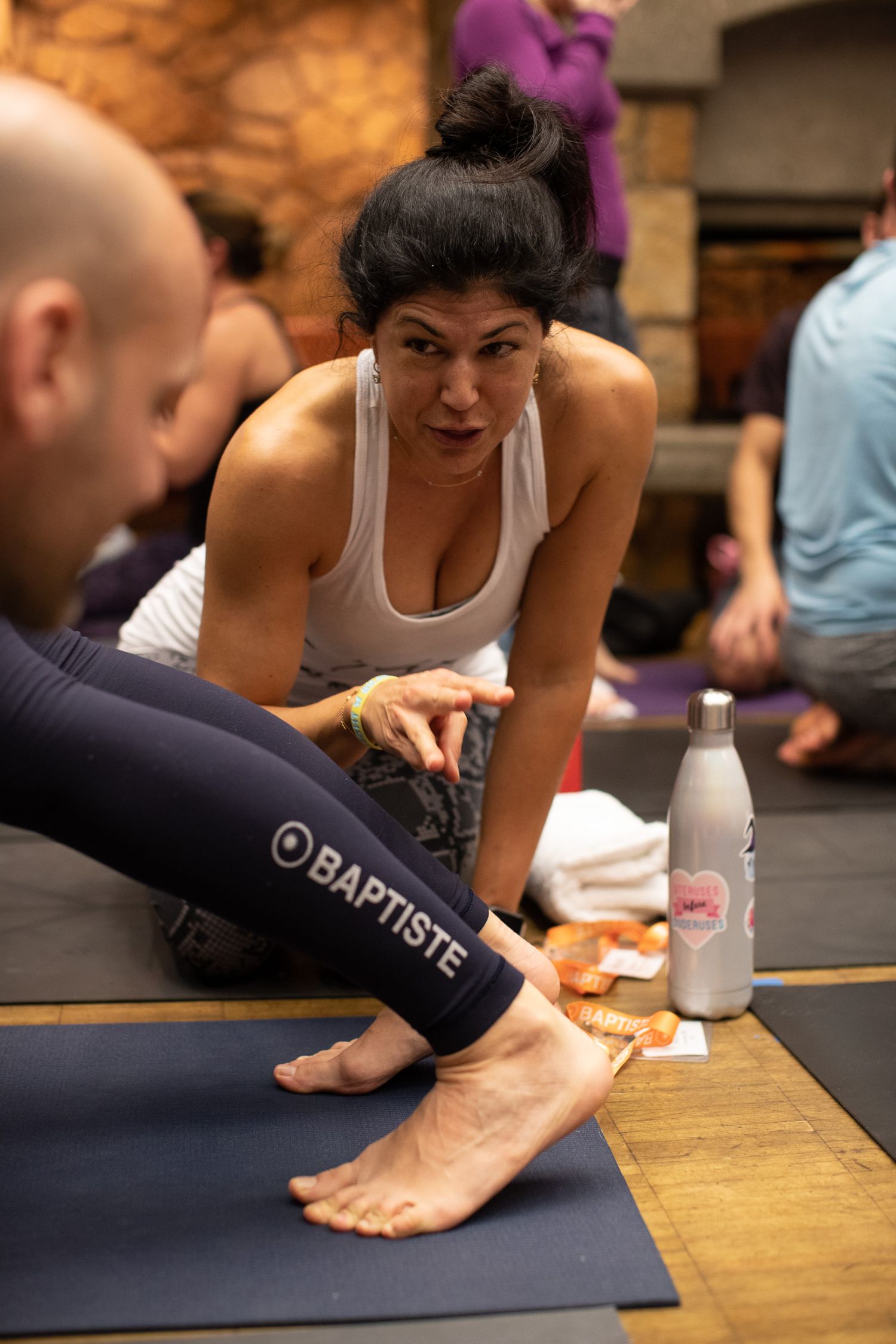 Yoga instructor assists student with foot positioning during a stretching exercise on a blue mat.