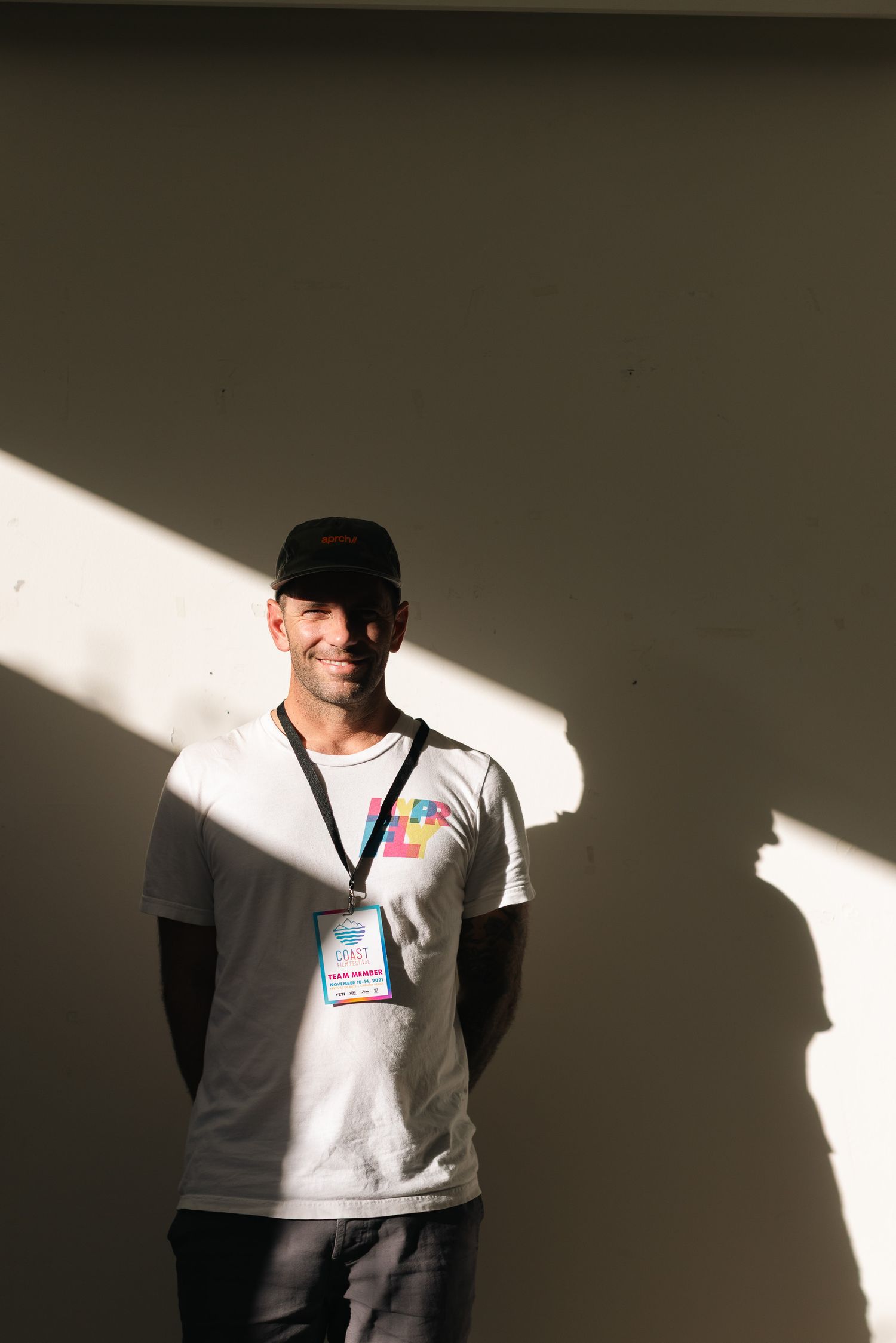 A person wearing a baseball cap is lit by dramatic side lighting against a dark background.