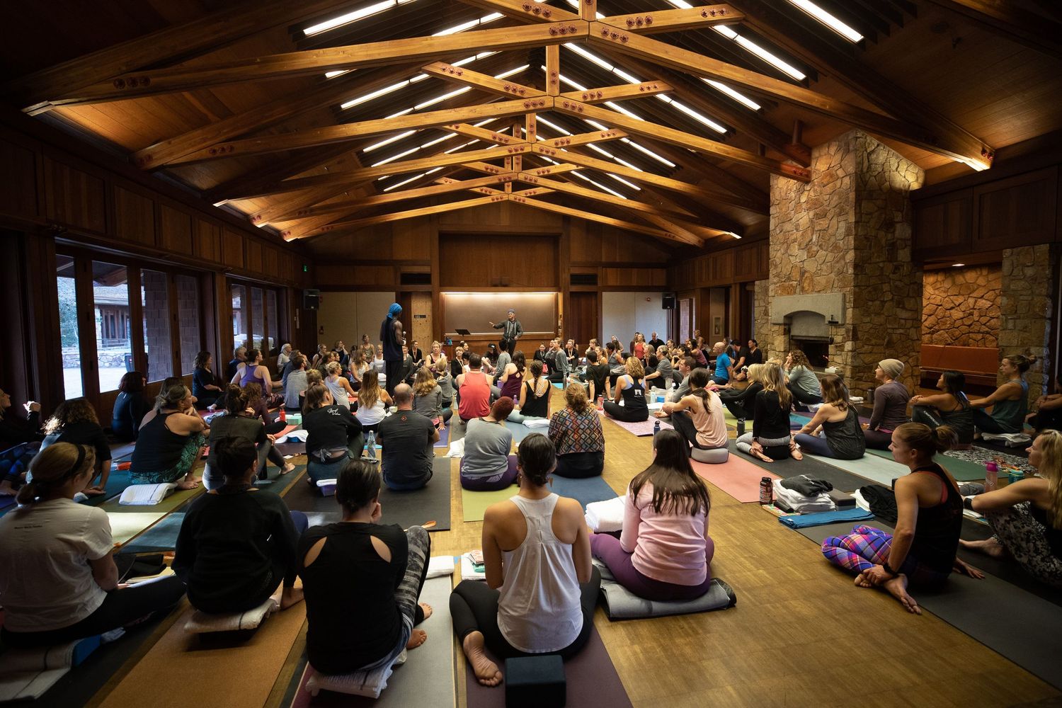 Large group of participants practicing yoga exercises in a rustic wooden room.