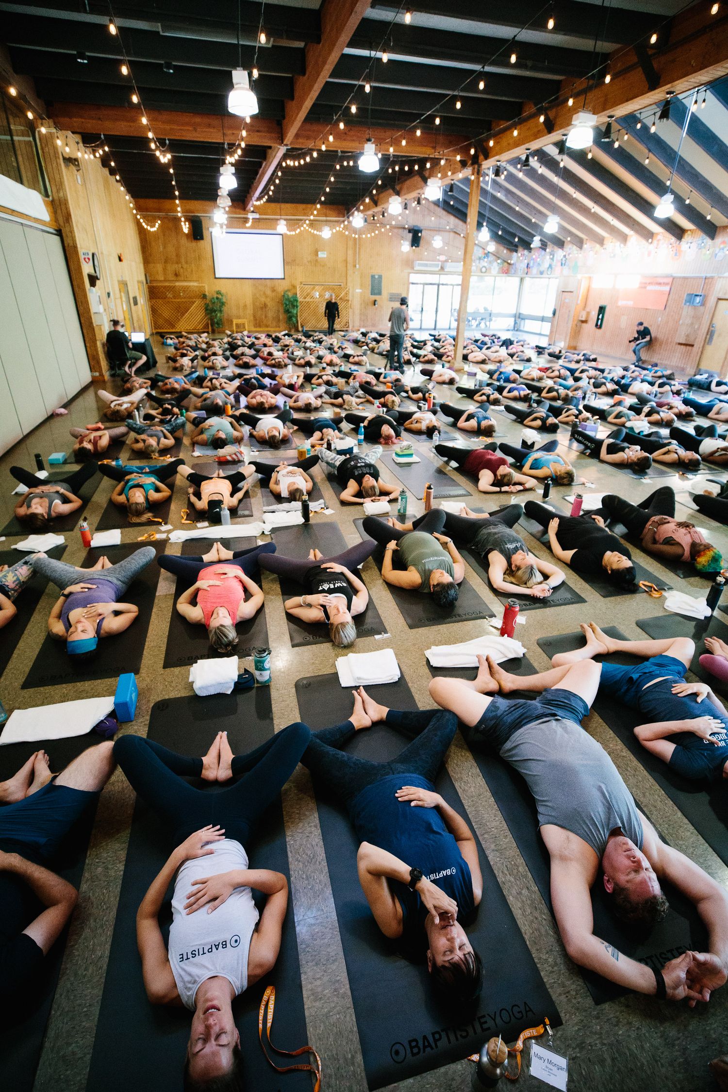 Crowded yoga studio with participants lying on mats during a group meditation session.