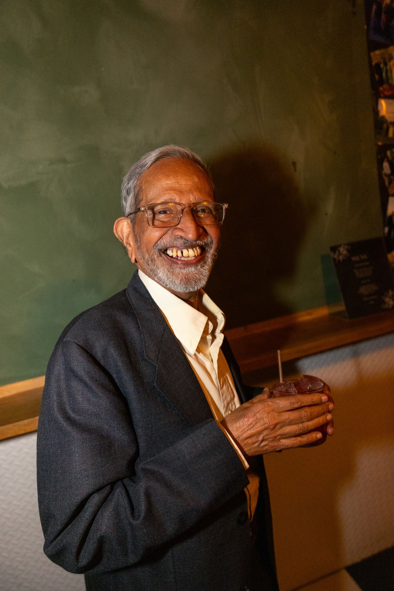 An elderly man in a dark suit jacket laughs joyfully during a celebration.