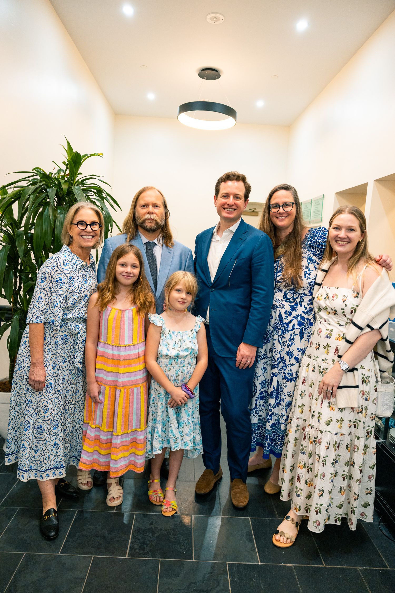 Group photo of people wearing floral dresses and formal attire standing in modern interior hallway.