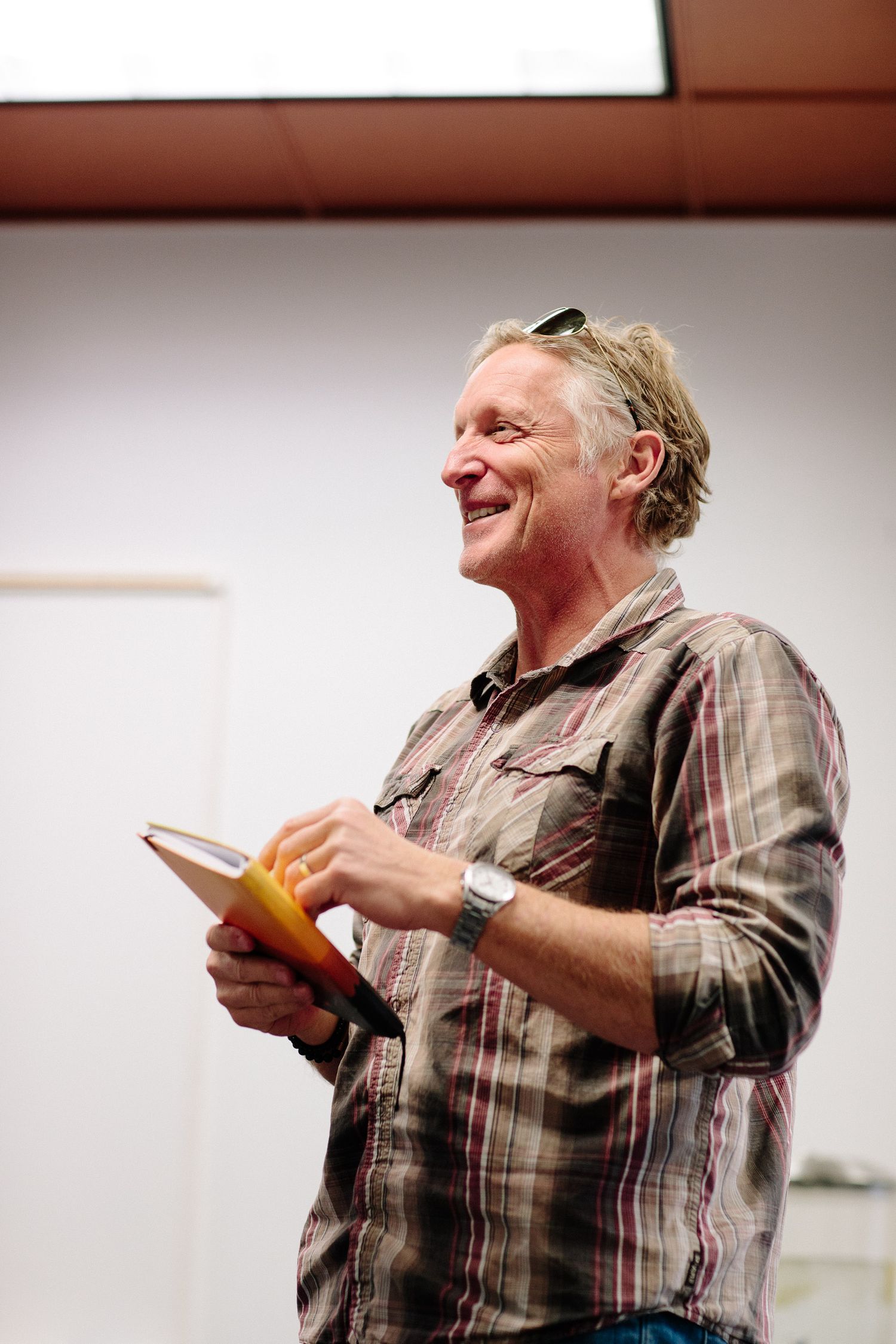 A person in a plaid shirt smiling while holding a notebook during a presentation.
