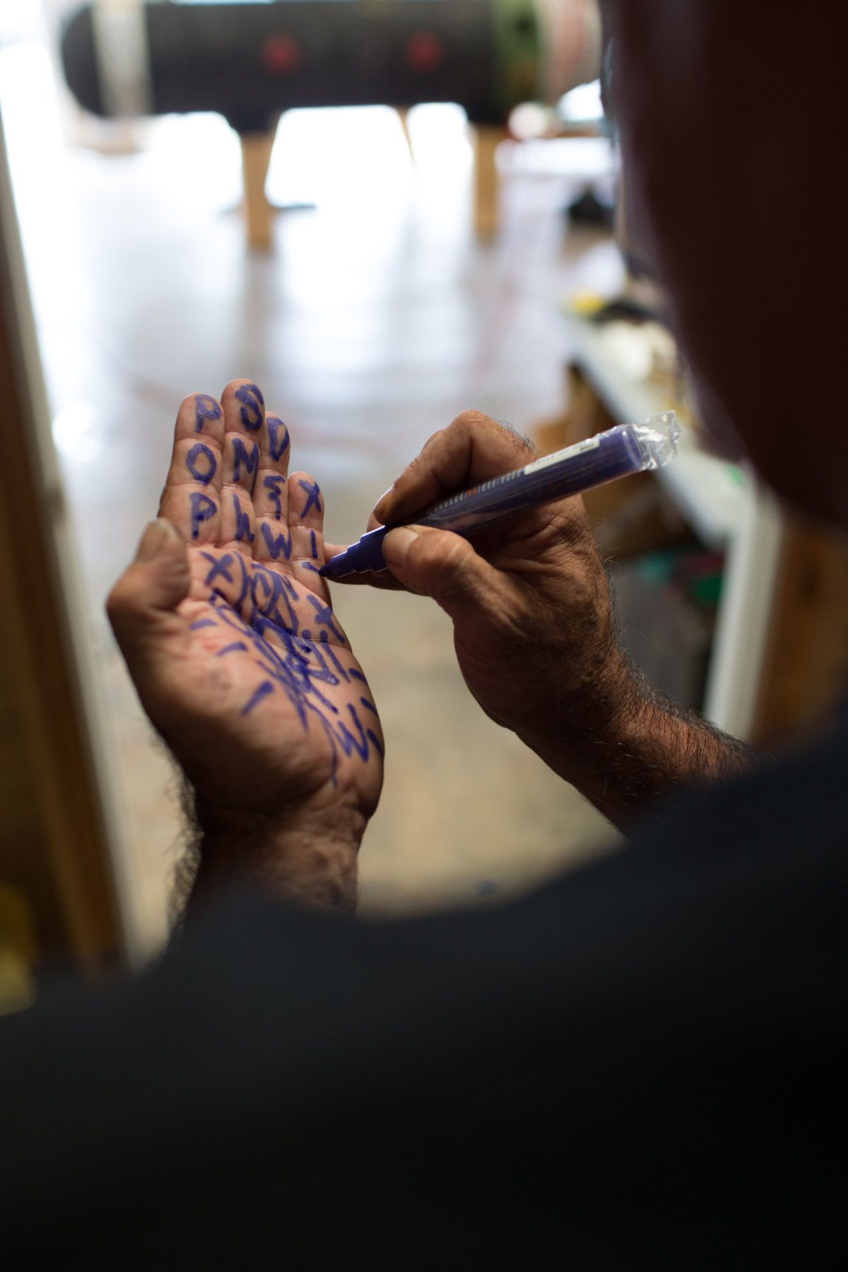 Close-up of hands writing blue text on palm with pen.