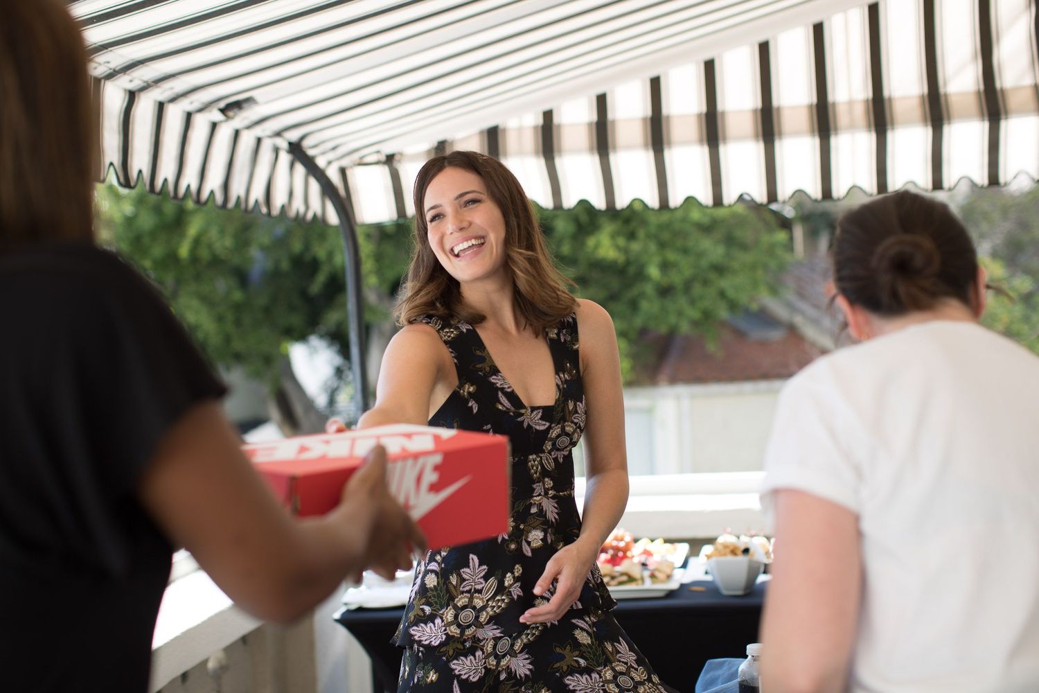 People chatting and socializing at an outdoor gathering under striped awning.
