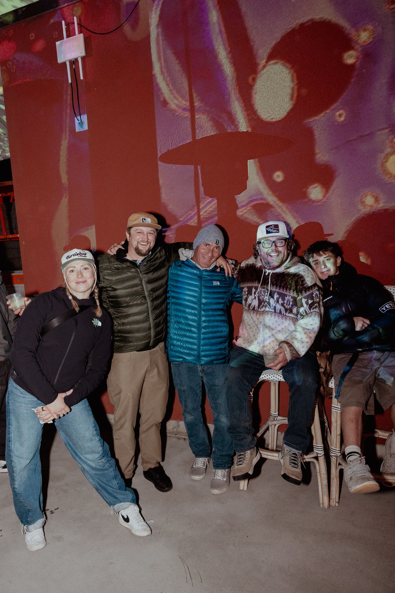Group of people in warm clothing lined up against a red-lit backdrop.