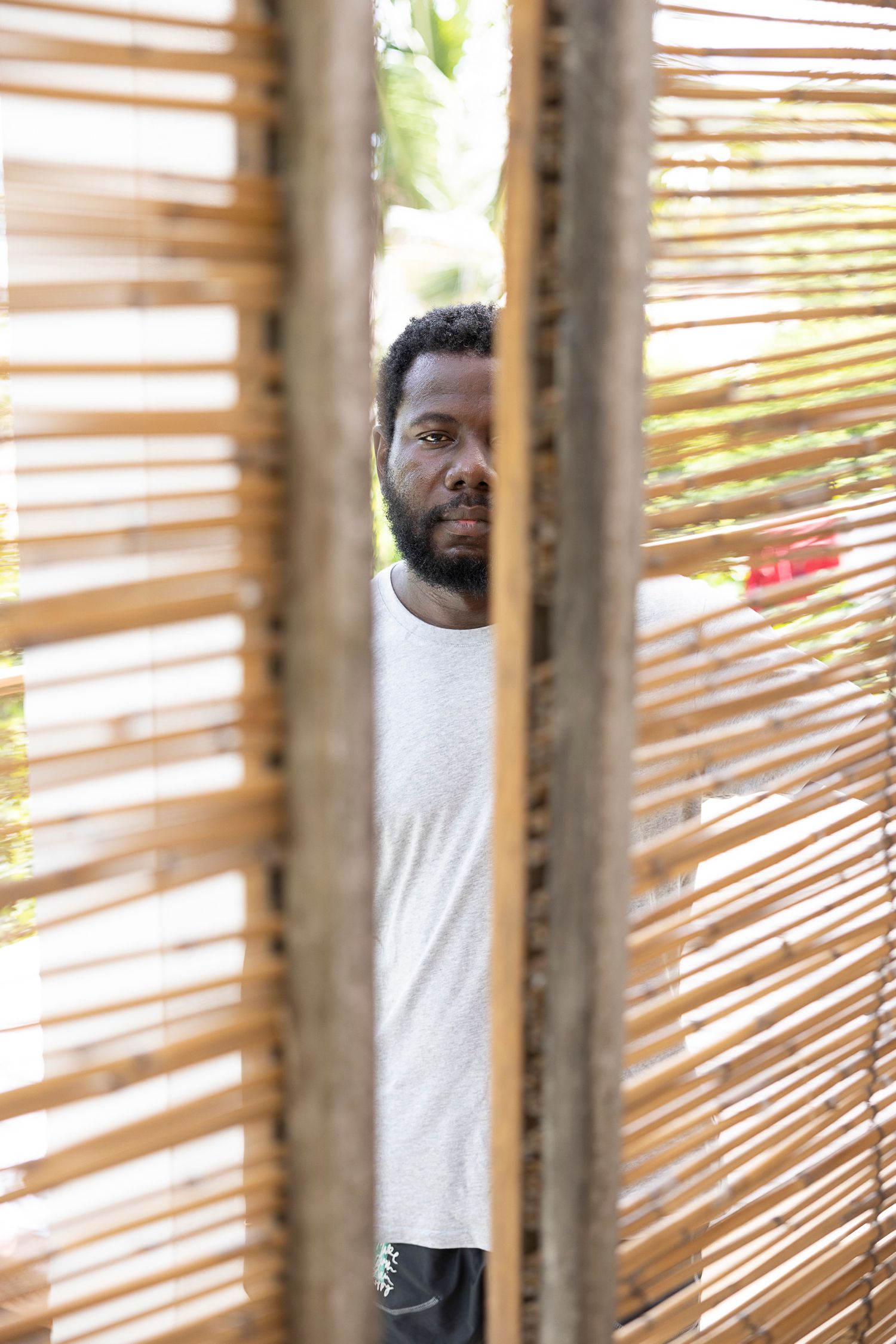 Someone peeks through wooden slat blinds while smiling, creating a playful striped pattern effect.