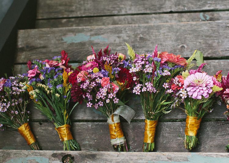 Colorful flower bouquets arranged in mason jars with yellow wrapping on a rustic wooden surface.