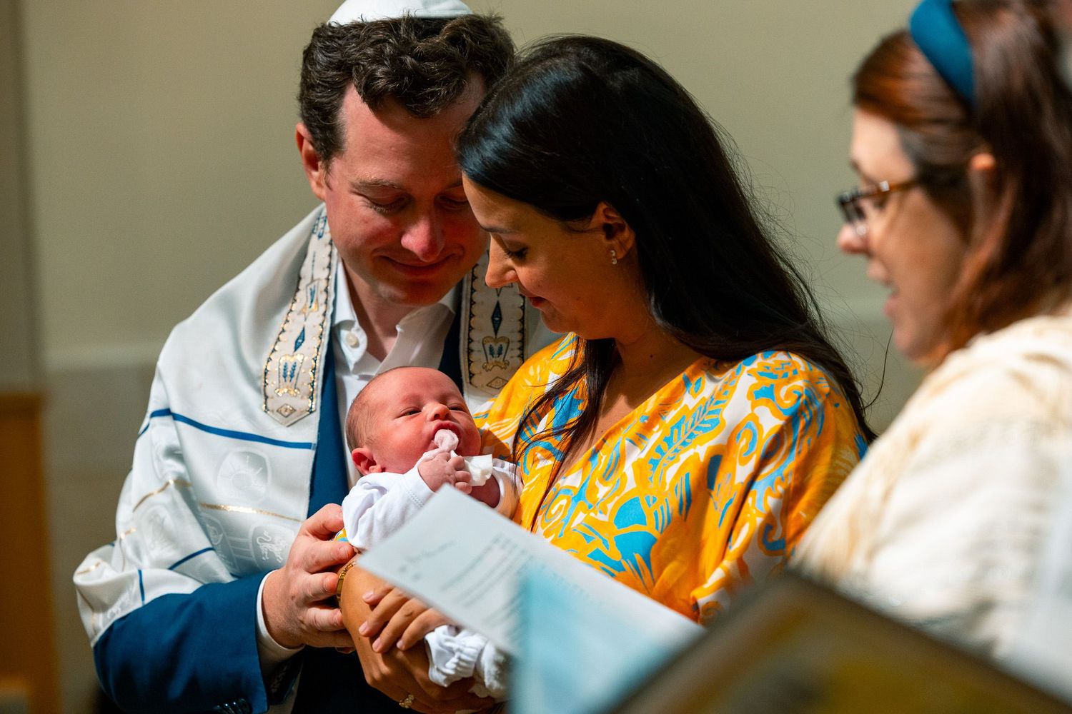 Parents holding their newborn baby during a religious ceremony in traditional attire.
