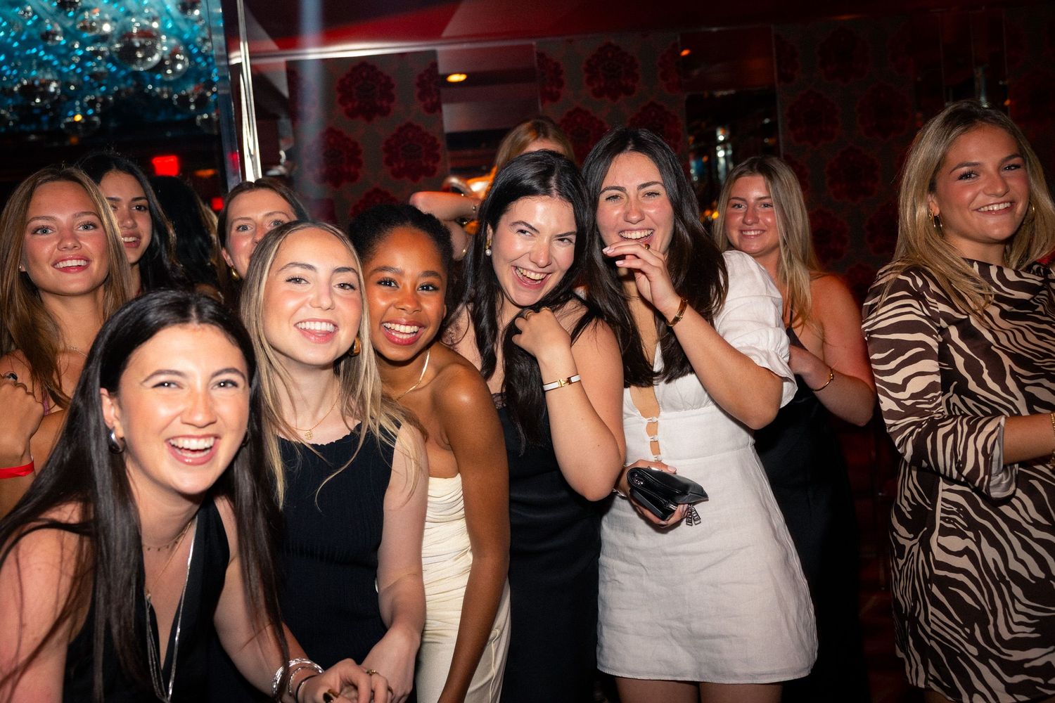 A group of friends in party dresses smile and laugh together at a nightclub.