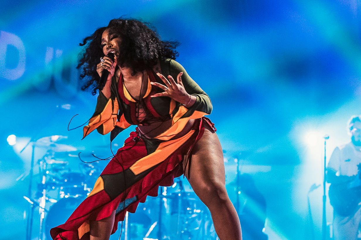 Energetic performer in orange outfit dances on stage with dramatic blue lighting.