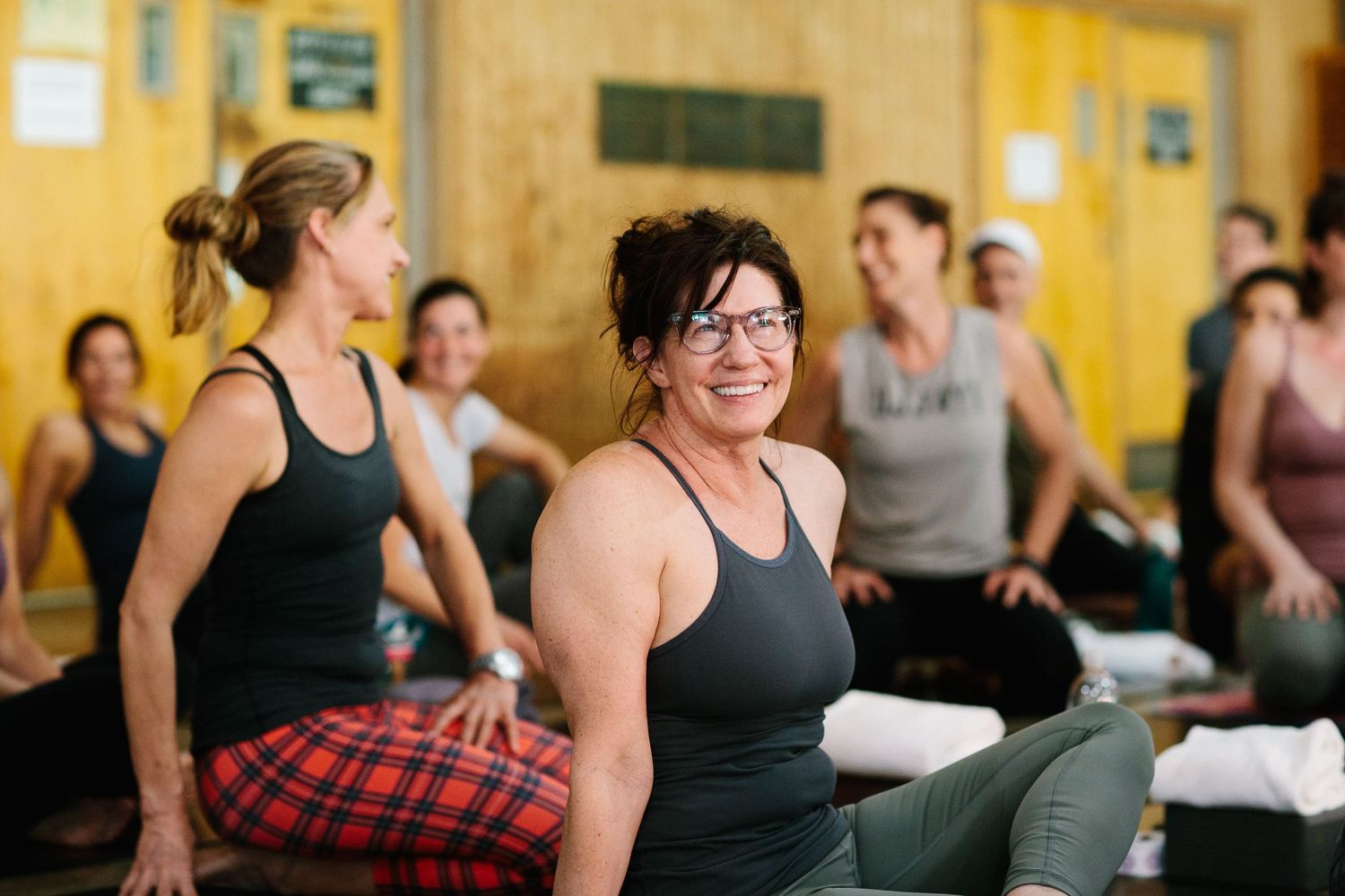 Students in workout attire smiling during break at fitness class with yellow walls in background.