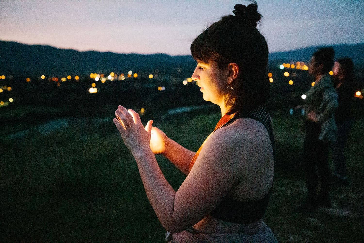 Silhouette of person holding glowing object at dusk with city lights in background.