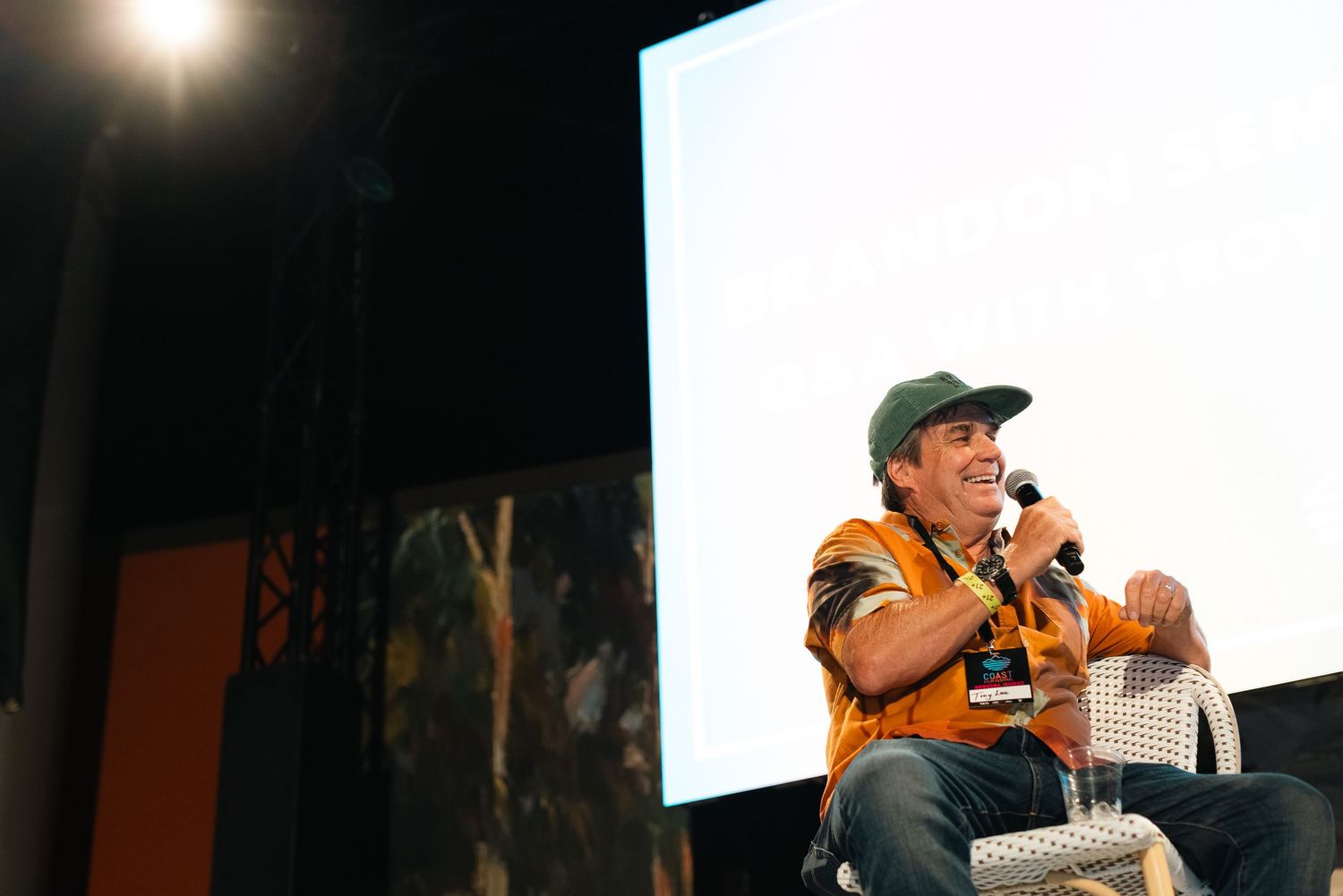 Event speaker on stage with projection screen visible in background.
