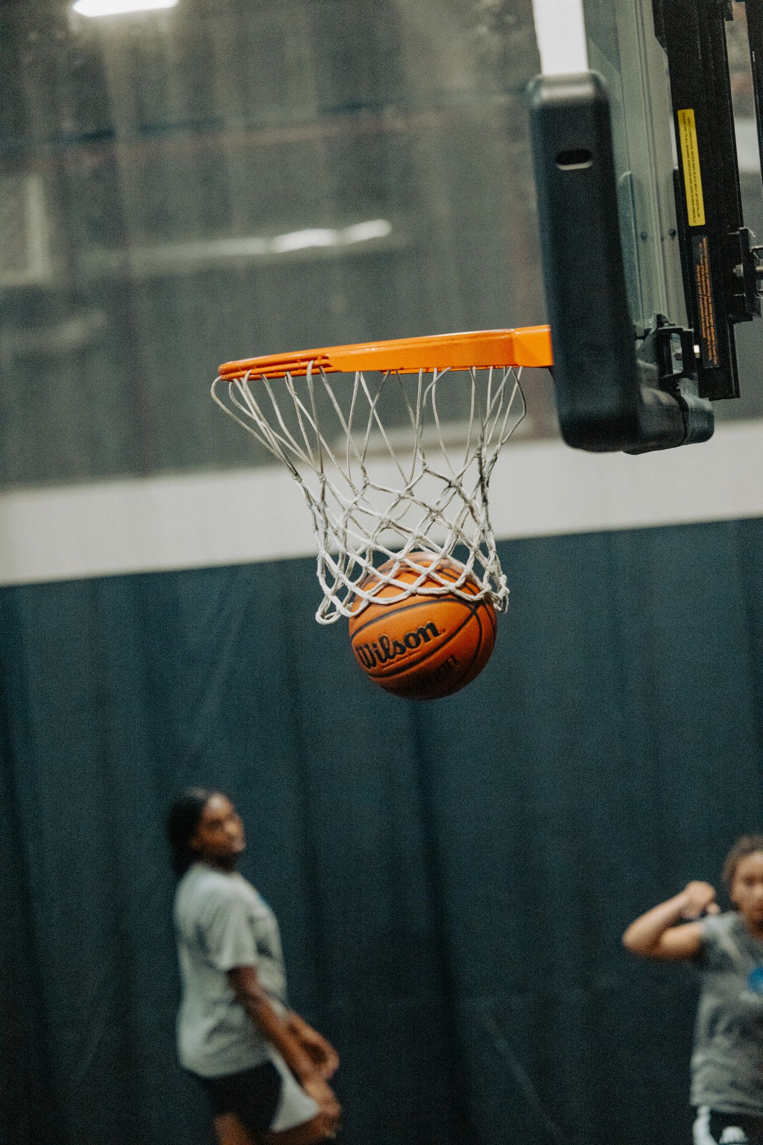 Basketball going through hoop with net and indoor court background.