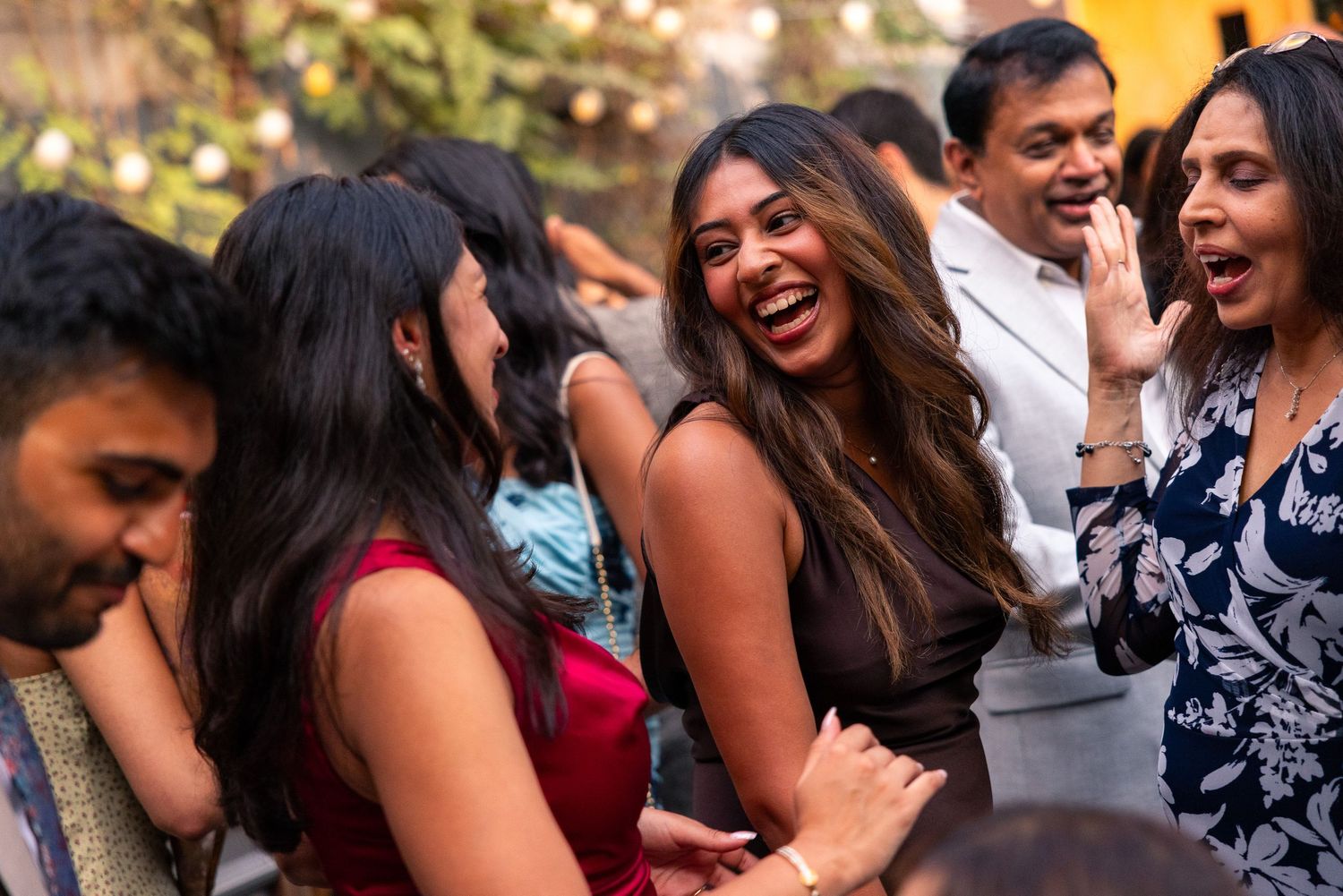 Happy group celebrating at outdoor party with string lights and laughter.